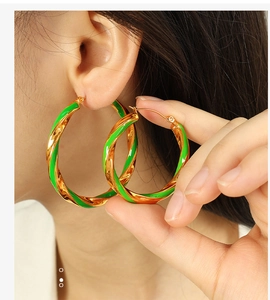 Macro detail of large gold-plated twist earrings featuring vibrant green enamel drips