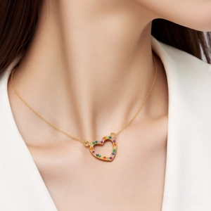 Close-up of a golden heart necklace featuring colorful micro-pave crystals on a model