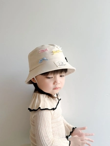 Detailed view of beige kids sun hat with colorful bows and embroidered patch accents