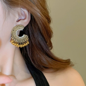 Close-up of ethnic gold C-shaped tassel earrings with pearls on model's ear