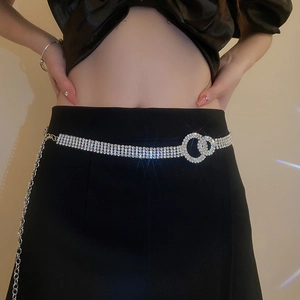 Dettaglio catena in vita con strass, fibbia a doppio anello e nappe metalliche su abito nero