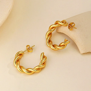 Close-up of 18k gold-plated twisted hoop earrings on a minimalist beige ceramic surface