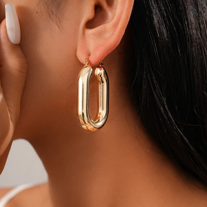 Detail view of a model wearing oval golden hoop earrings with a smooth metallic finish