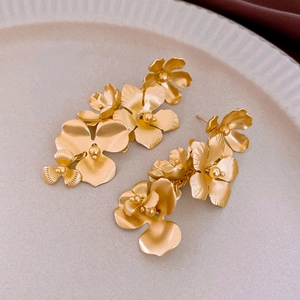 Macro detail of matte gold flower earrings with layered petals on a beige tray