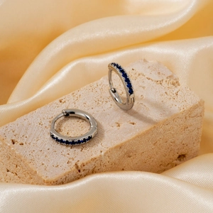 Detail of silver hoop earrings with blue zircon inlays on a textured stone base
