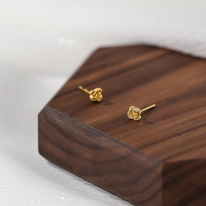 Elegant gold S999 sterling silver rose stud earrings displayed on a rustic wooden stand