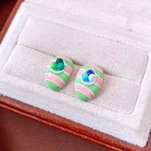 Macro detail of oval striped stud earrings with micro beads in a beige jewelry box