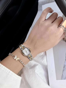 Close-up of a square gold and silver steel watch with pearl butterfly bracelet and ring
