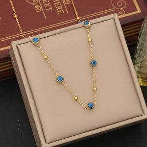 Detail of gold evil eye necklace with blue enamel charms on a beige jewelry display