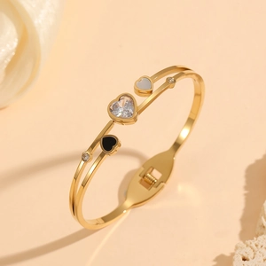 Détail du bracelet doré avec zircons et breloques en forme de cœur noir et blanc