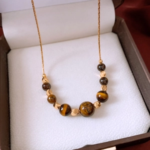Macro shot of 18k gold-plated chain and tiger eye beads in a luxury jewelry box