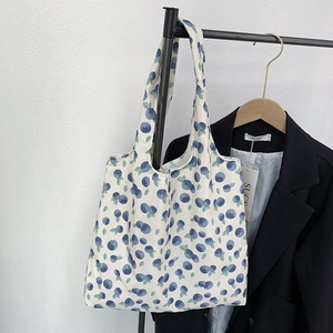 Detail of white canvas tote bag featuring blue berry floral patterns hanging on a hanger