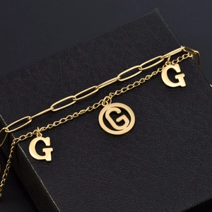 Double-layered gold titanium steel bracelet featuring cutout G pendants on a black background