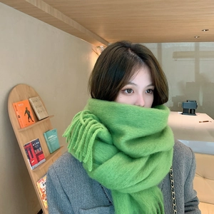 Close-up of soft green mohair scarf with tassels worn in a cozy cafe setting