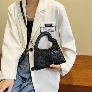 Detail of a black heart-shaped handbag with crocodile texture and unique cut-out handle
