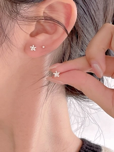 Macro shot of minimalist silver flower stud earrings showing detail on ear