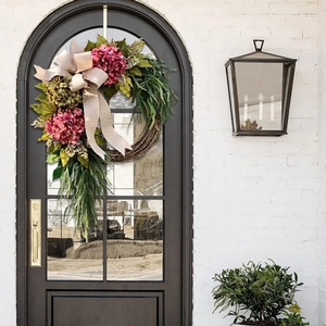 Detail of pink hydrangea wreath with burlap bow on a dark arched front door