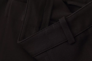 Κοντινό πλάνο υφής μαύρου υφάσματος twill και λεπτομέρειες ραφής στη ζώνη του παντελονιού