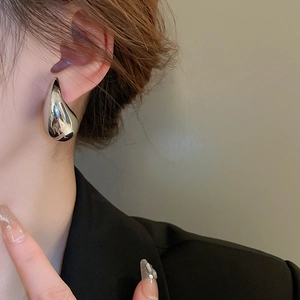 Close-up of a silver water drop earring worn by a model in a black suit