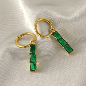 Boucles d'oreilles pendantes en acier titane doré avec zircons émeraude sur fond de soie