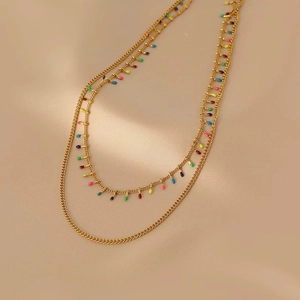 Detail of double-layer gold titanium necklace with colorful enamel charms on beige surface