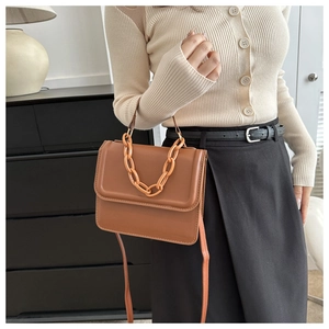 Brown leather crossbody bag with resin chain handle shown styled with casual knitwear