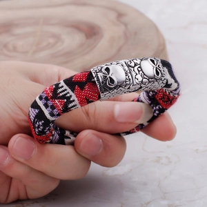 Detail of woven rope bracelet with silver skull charm and floral pattern buckle