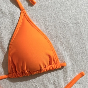Detail of vibrant orange triangle bikini top with drawstring ties on white linen fabric
