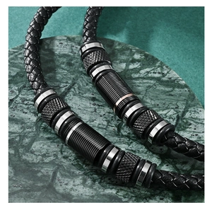Macro detail of men's black woven leather bracelet with textured metal charms