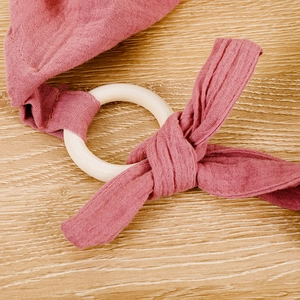 Close-up of pink cotton muslin fabric tied to a natural wooden ring for baby