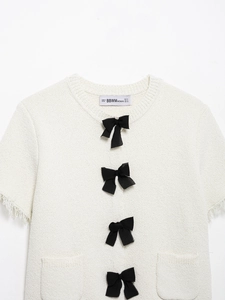 Nahaufnahme des weißen Tweed-Cardigans mit schwarzen Schleifen und Fransenrand
