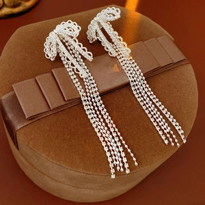 Close-up of silver bow tassel earrings with zircon crystals on a brown velvet gift box