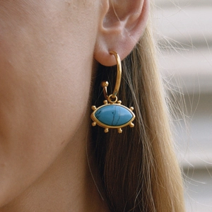 Close-up of gold evil eye hoop earring with turquoise stone on model's ear
