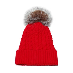 Detail of red cable-knit beanie featuring a fluffy grey-brown faux fur pompom detail