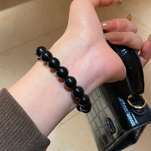 Detailed view of polished black obsidian bead bracelet on wrist with elegant bag background