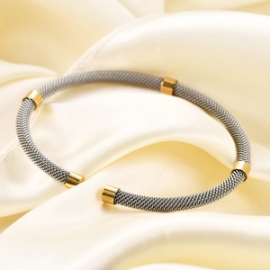 Detail of woven stainless steel cable bracelet with gold-plated accents on silk background