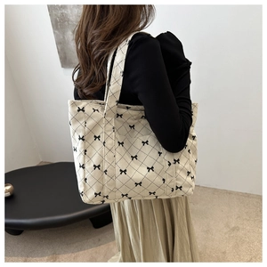 Detailed close-up of beige corduroy tote bag with black bow and quilted pattern design
