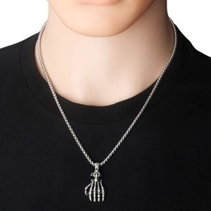 Détail d'un pendentif crâne main squelette porté sur une chaîne box en acier inoxydable