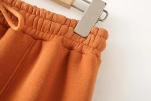 Detail view of orange sports pants featuring elastic knit waistband and drawstring