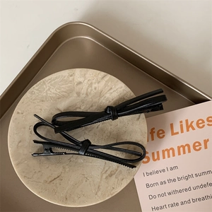 Close-up of black faux leather bow hair clips on a marble coaster and tray