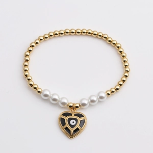 Golden beaded evil eye heart pendant bracelet with white pearls on a minimalist background