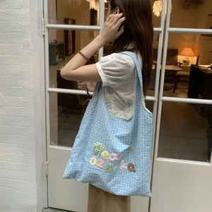 Detail of light blue quilted tote bag with colorful 3D letters on model's shoulder