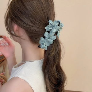 Détail de la pince à cheveux fleurs en tissu bleu clair sur cheveux ondulés bruns