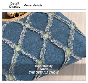 Close-up of blue denim shell bag showing frayed diamond pattern and pearl clasp detail