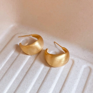 Macro view of golden C-shape earrings with brushed matte finish on beige texture