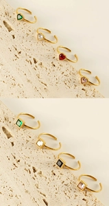 Close-up of colorful heart and square gemstone rings on a textured stone display