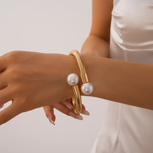 Detail of a gold metallic flexible collar with two large pearls worn by a model
