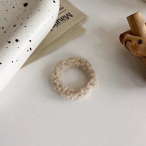 Dettaglio dello scrunchie in peluche beige morbido con trama in lana di agnello