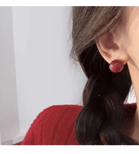 Close-up of a model wearing minimalist dark red spherical stud earrings with a matte finish