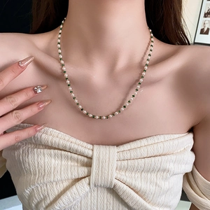 Nahaufnahme einer eleganten Goldkette mit weißen Perlen und grünen Perlen an einem Model